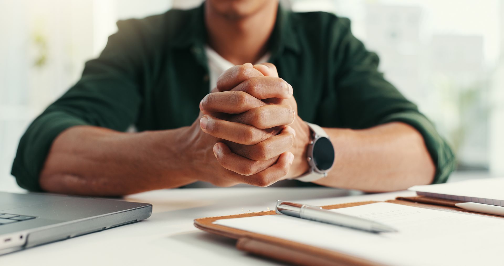 A man is sitting at a table with his hands folded.