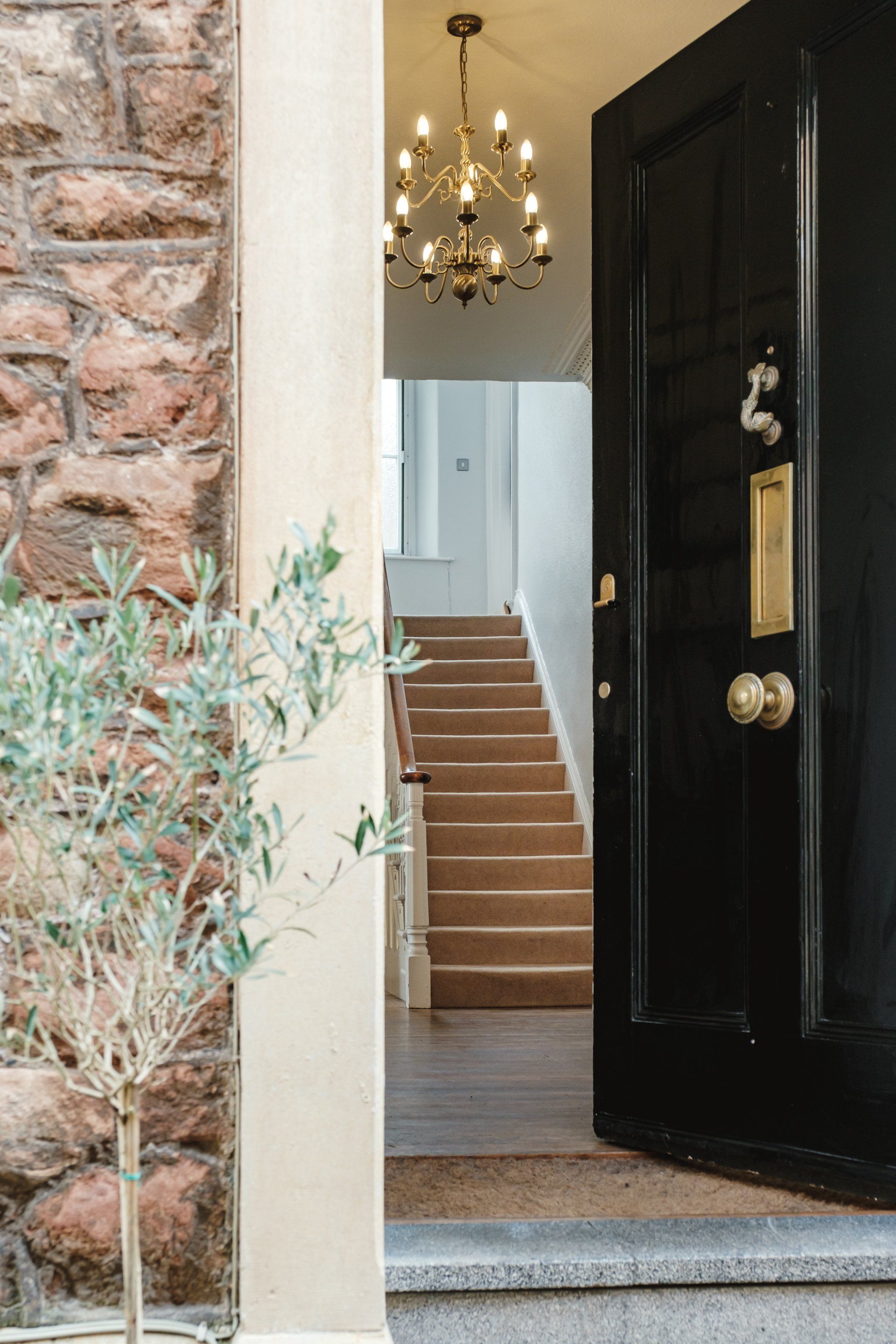 A black door is open to a hallway with stairs and a chandelier.