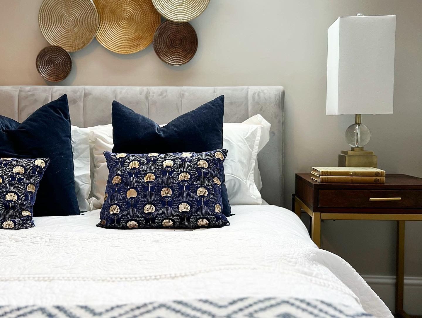 A bedroom with a bed , nightstand , lamp and pillows.