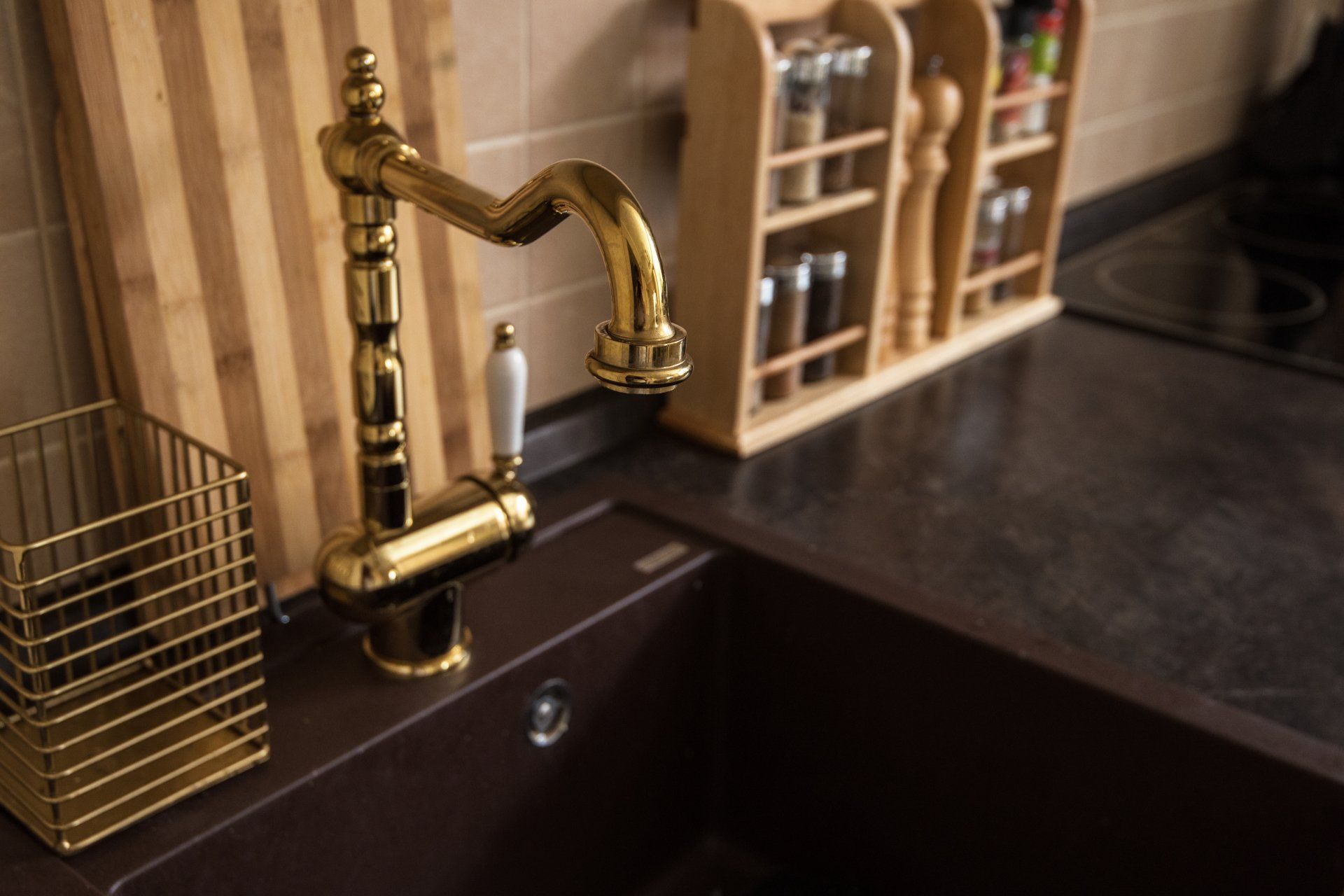 A kitchen sink with a gold faucet and a wooden cutting board.