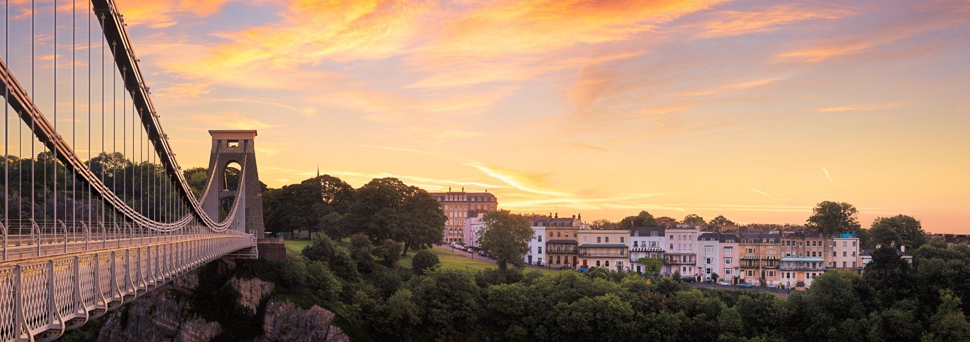 A bridge over a river at sunset with a city in the background.