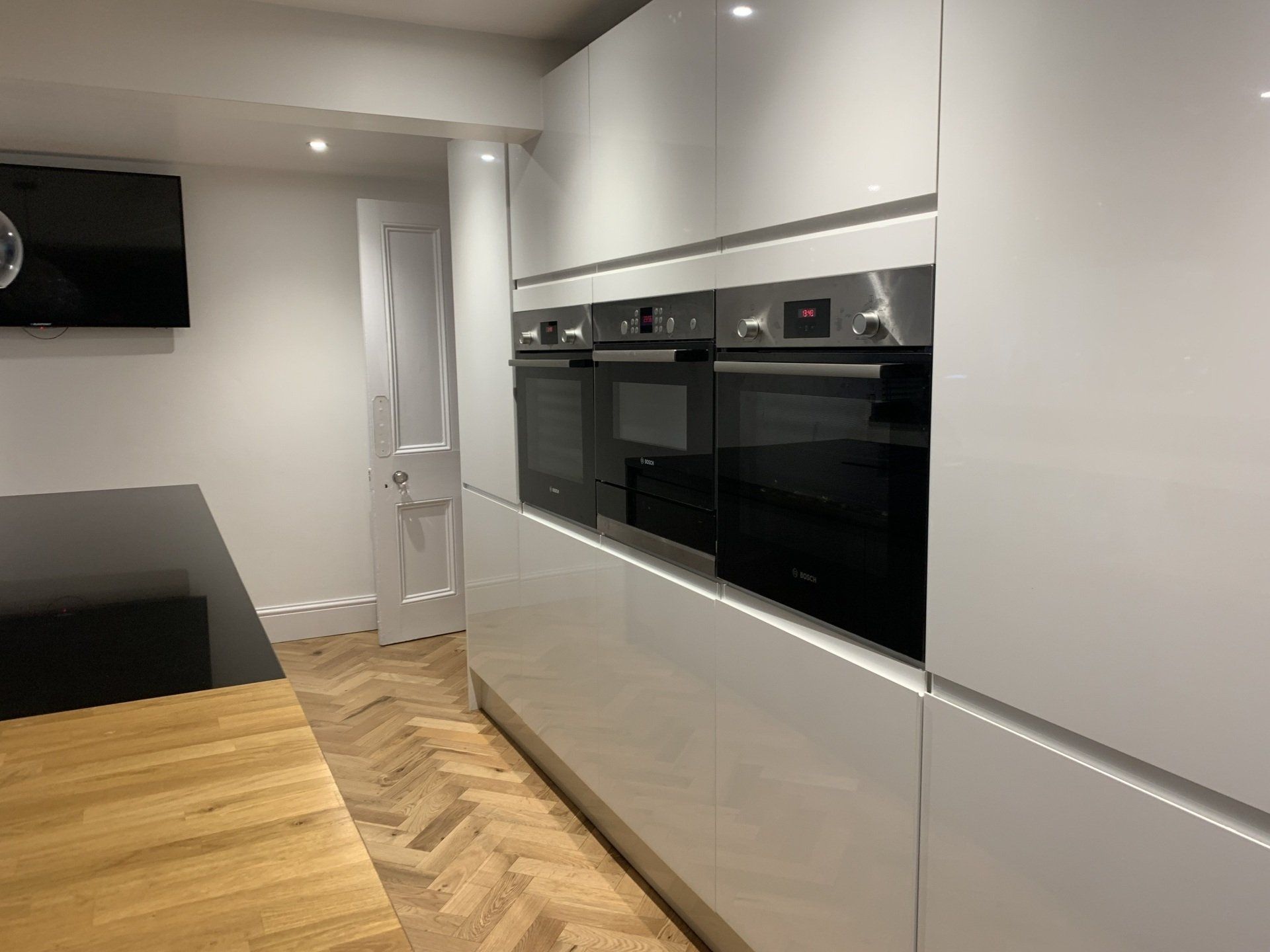 A kitchen with white cabinets and black appliances and a wooden floor.