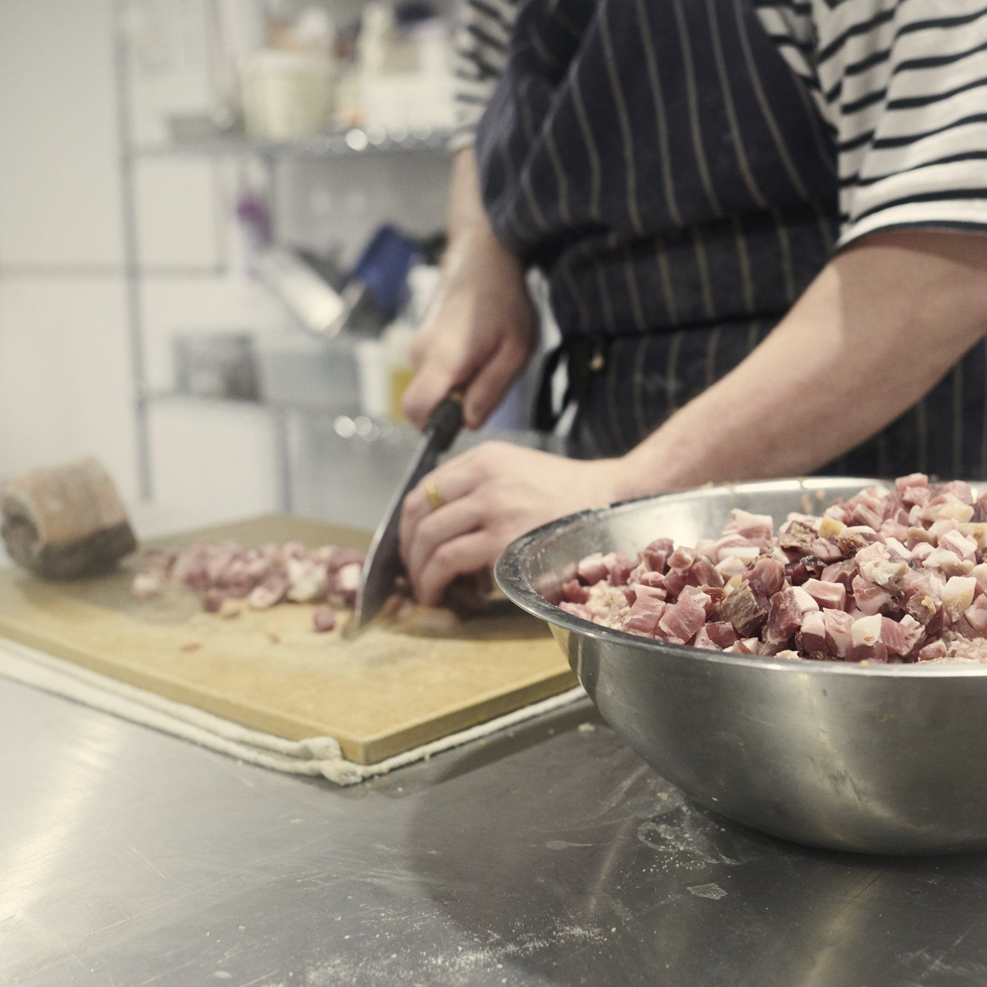 A person is cutting meat on a cutting board next to a bowl of meat