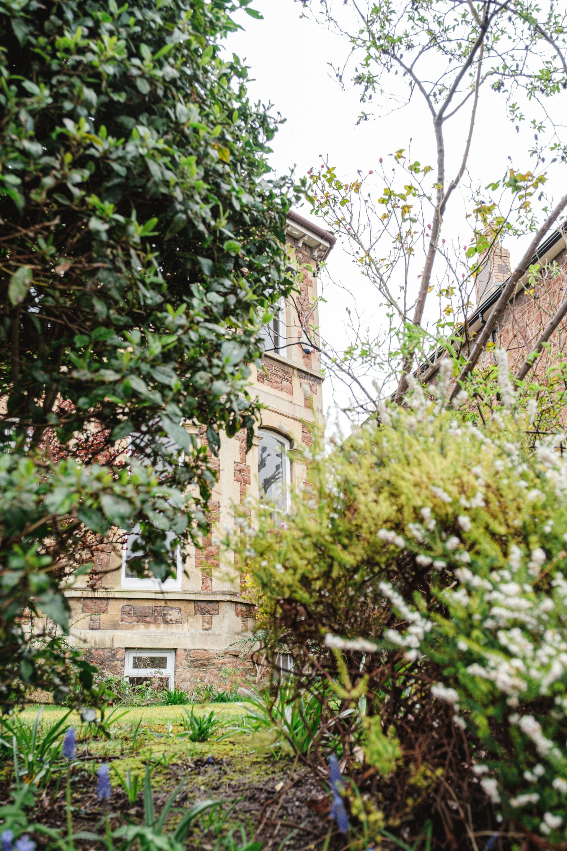 A large house is surrounded by trees and bushes in a garden.