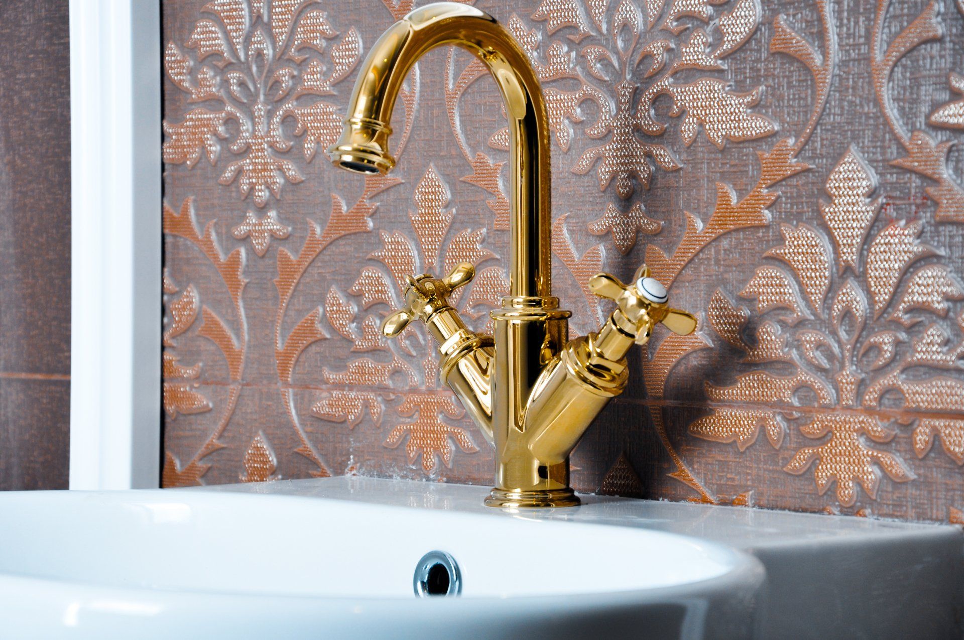 A gold faucet is sitting next to a white sink in a bathroom.