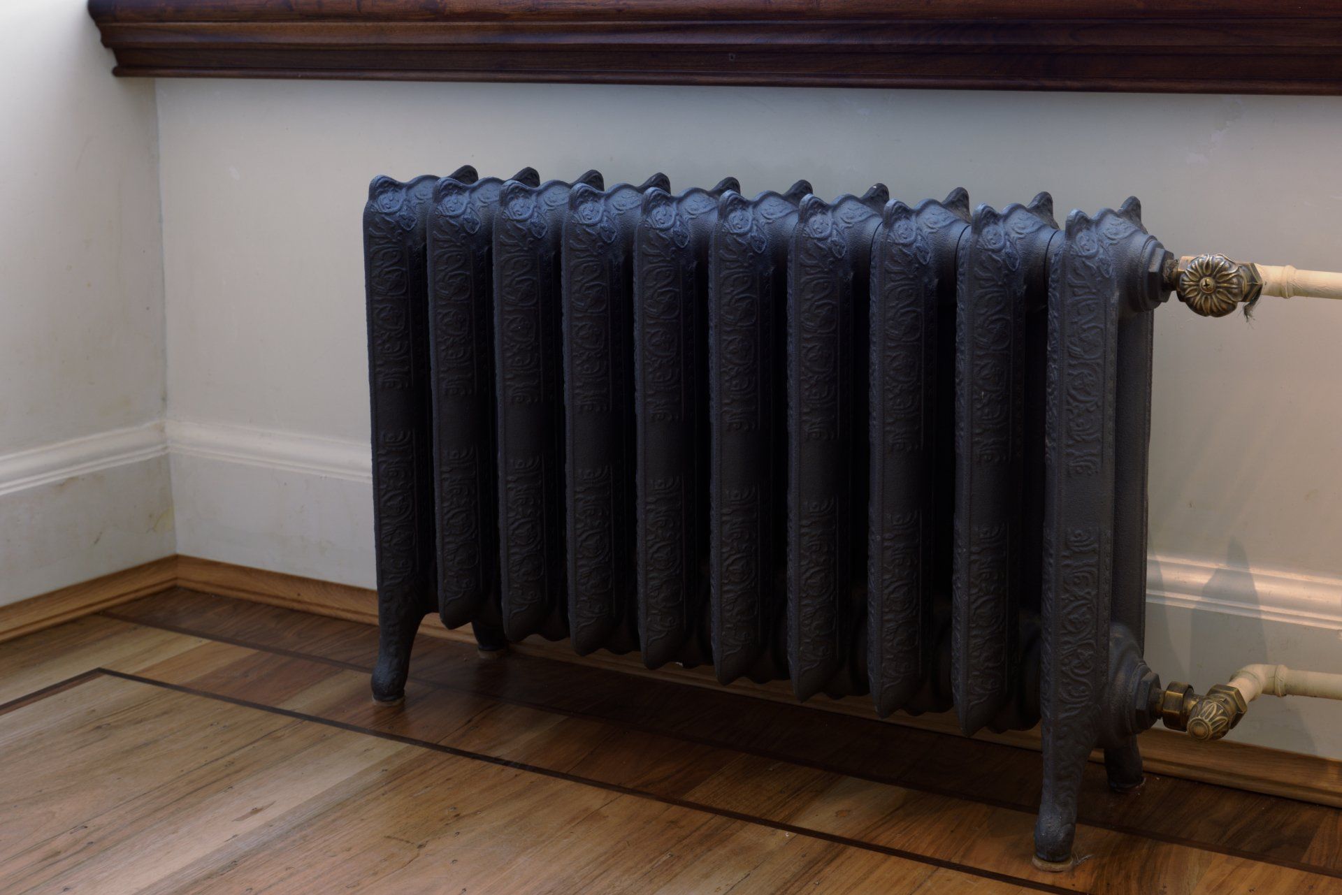A black radiator is sitting on a wooden floor in a corner of a room.