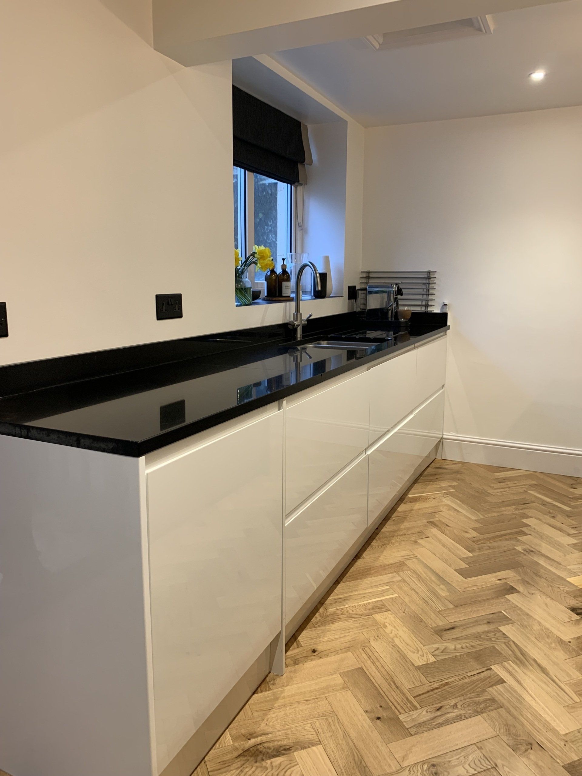 A kitchen with black counter tops and white cabinets and a herringbone floor.