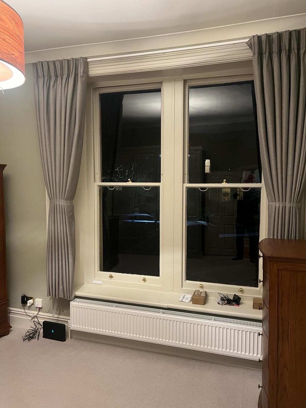 A bedroom with two windows , a radiator , and a lamp.