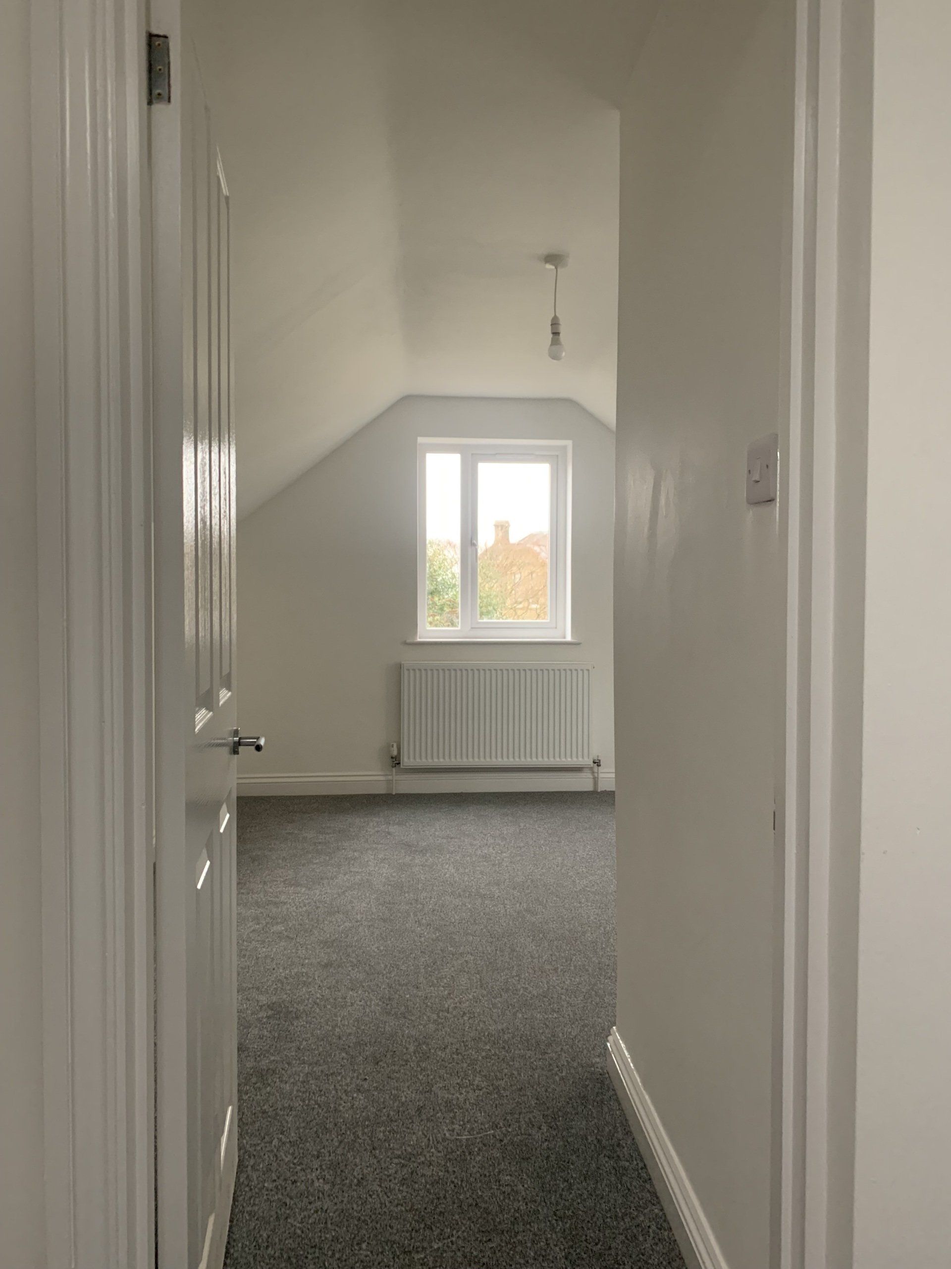 A hallway leading to an empty room with a window and a radiator.