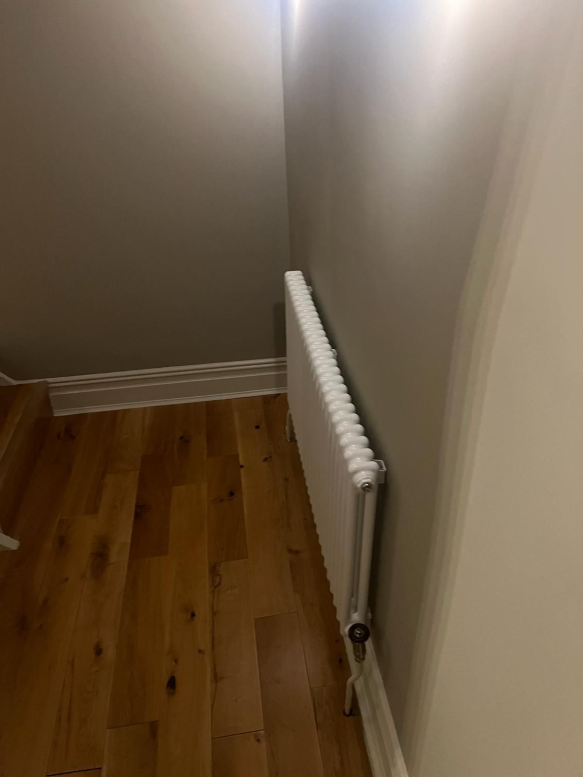 A white radiator is hanging on a wall in a room with hardwood floors.