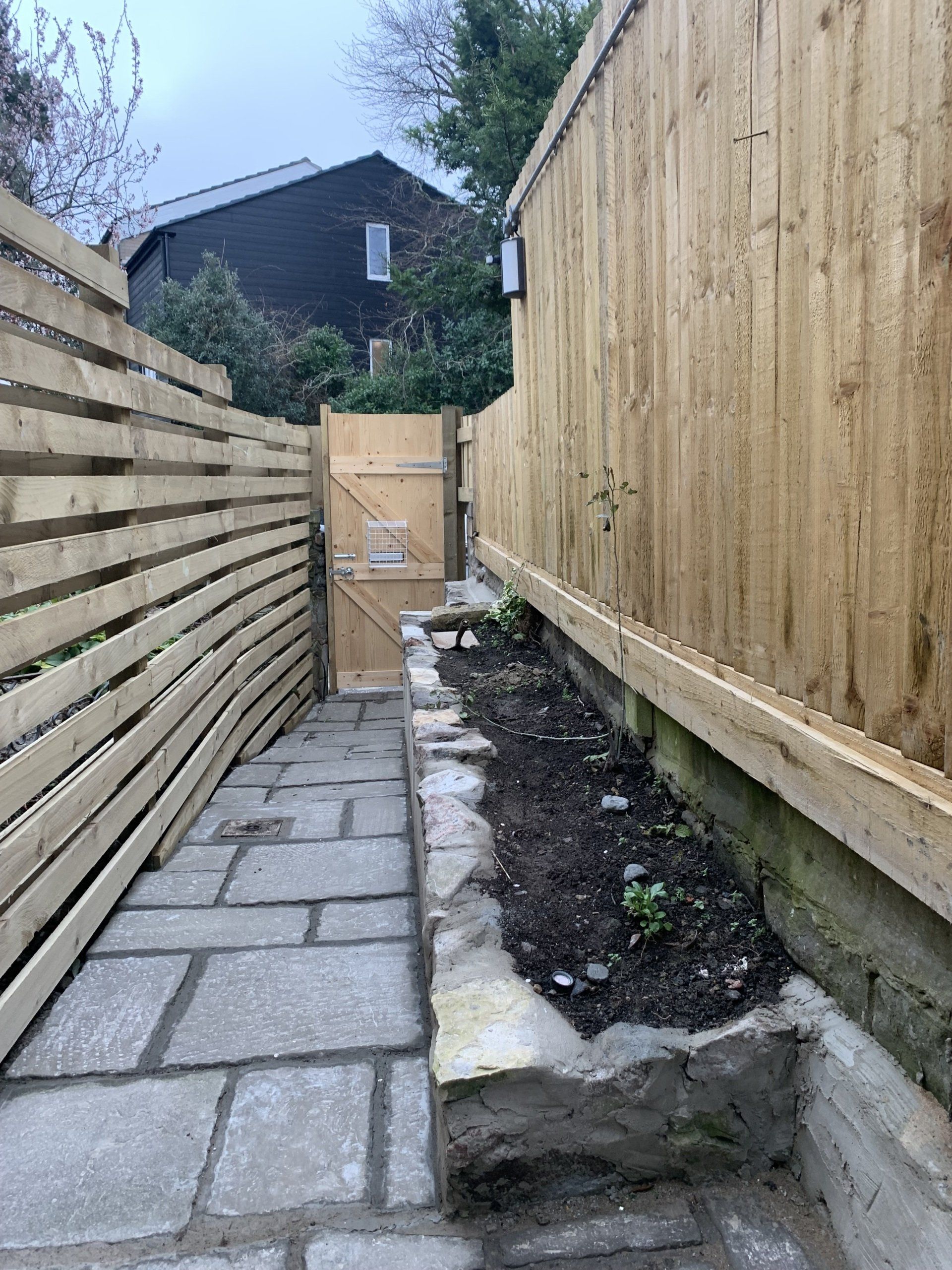 A wooden fence surrounds a stone walkway leading to a gate.