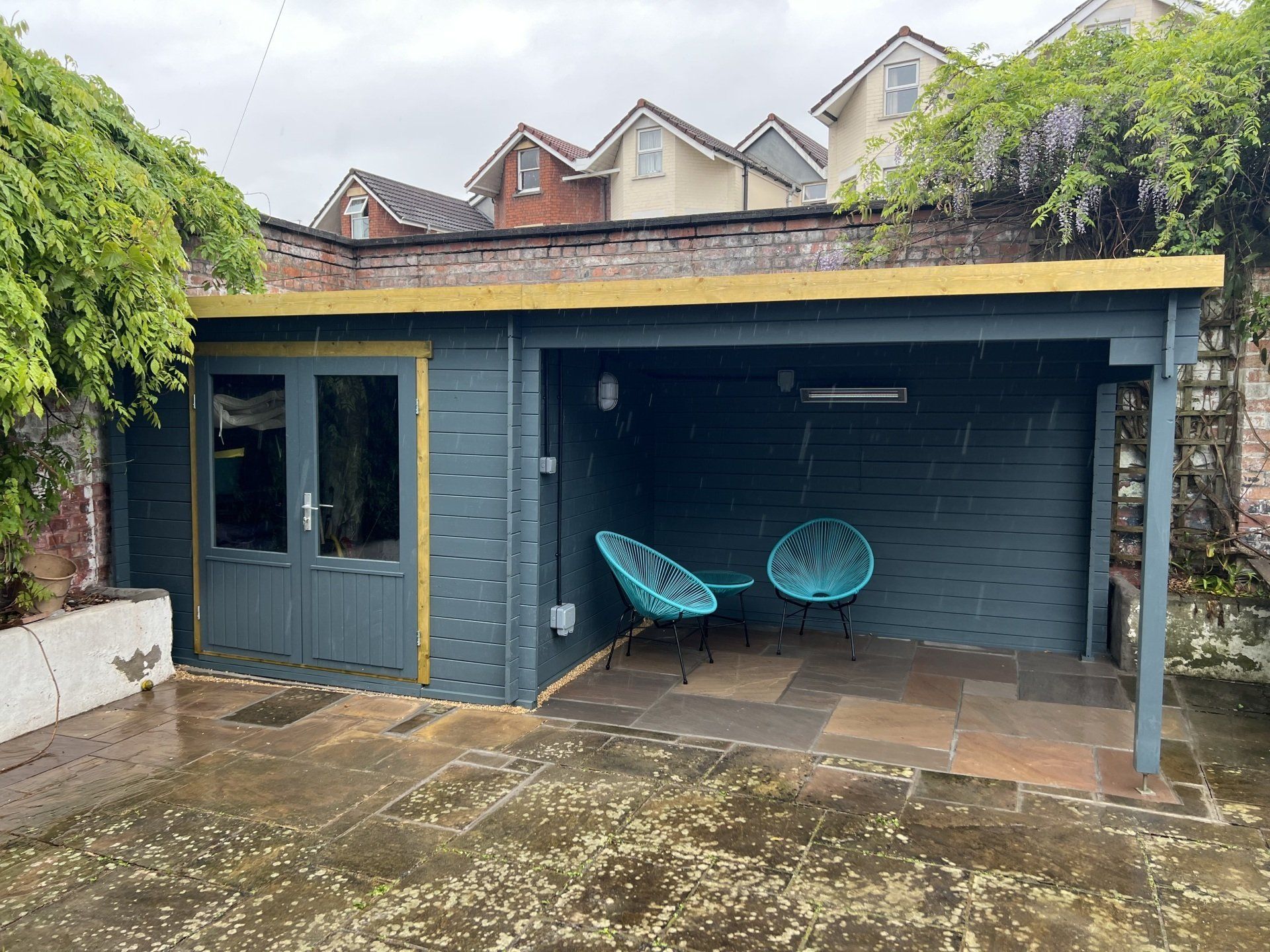 A blue shed with two chairs underneath it in a backyard.