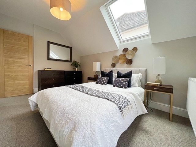 A bedroom with a bed , dresser , nightstand , mirror and skylight.