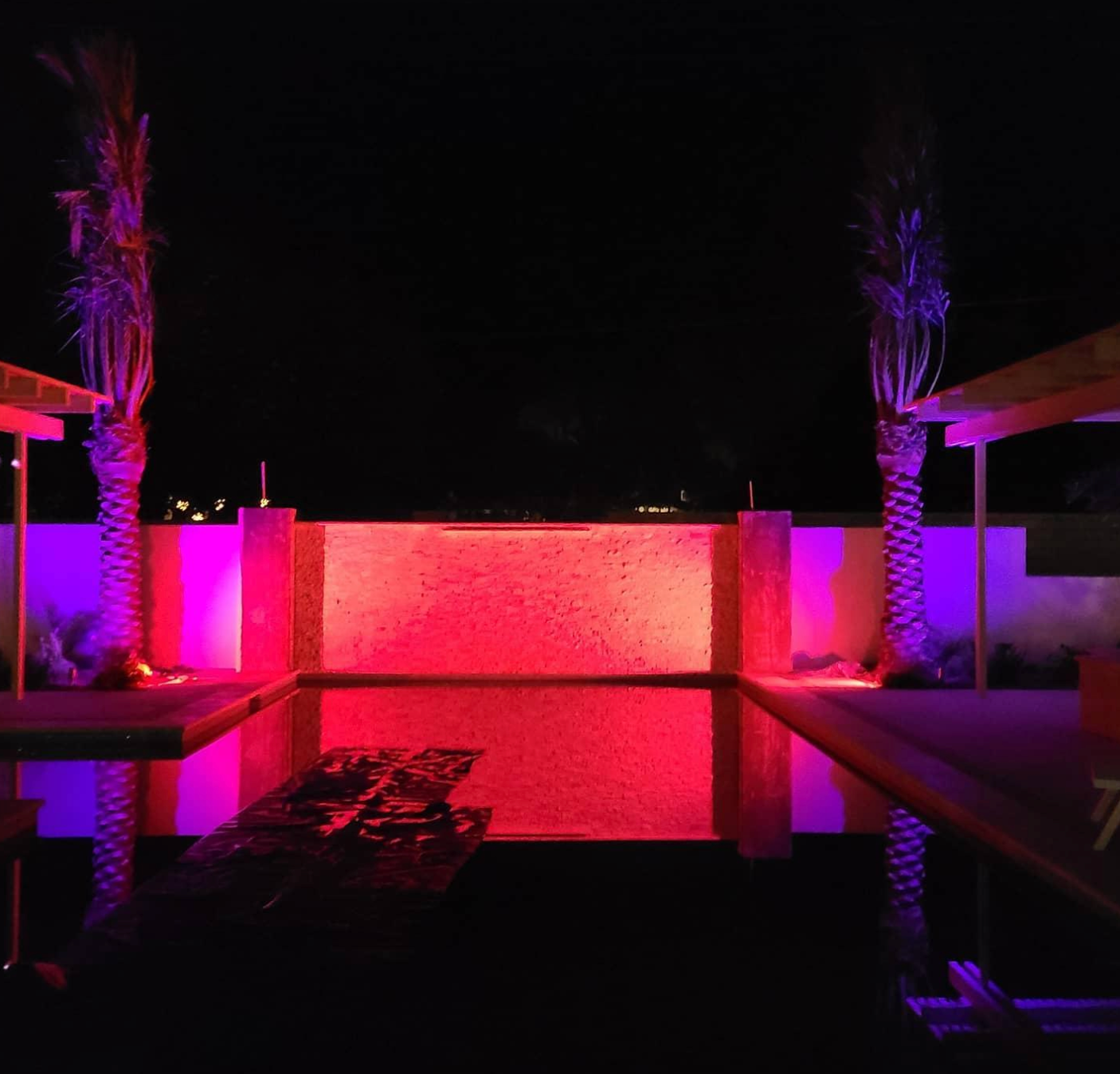 A swimming pool is lit up with pink and purple lights at night.