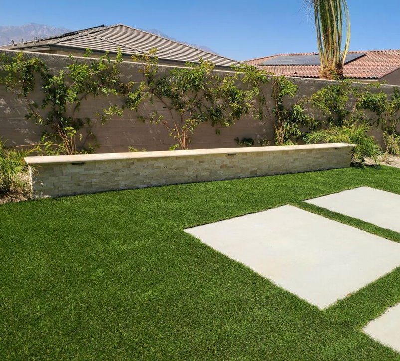 A lawn with a brick wall and a bench in the middle of it.