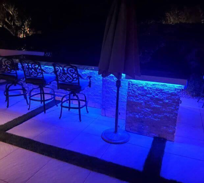 A patio with chairs and umbrellas lit up with blue lights.