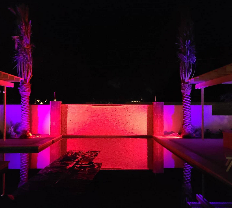 A swimming pool is lit up with pink and purple lights at night.