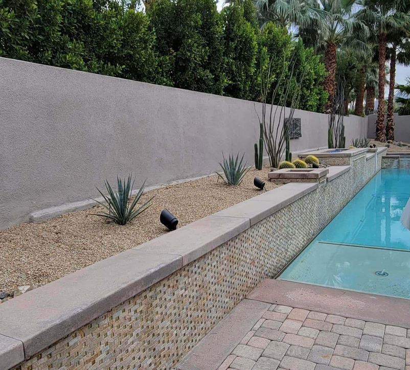 A swimming pool surrounded by plants and a brick walkway