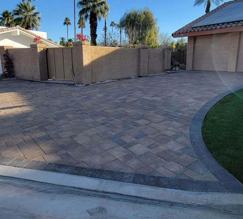 A brick driveway leading to a house with palm trees in the background.