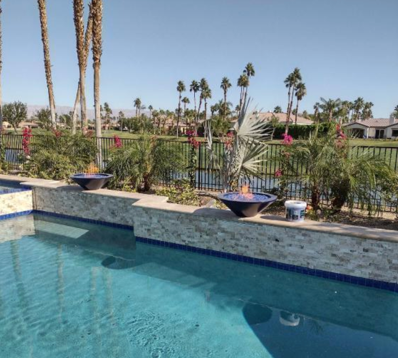 A swimming pool with a fire pit and palm trees in the background