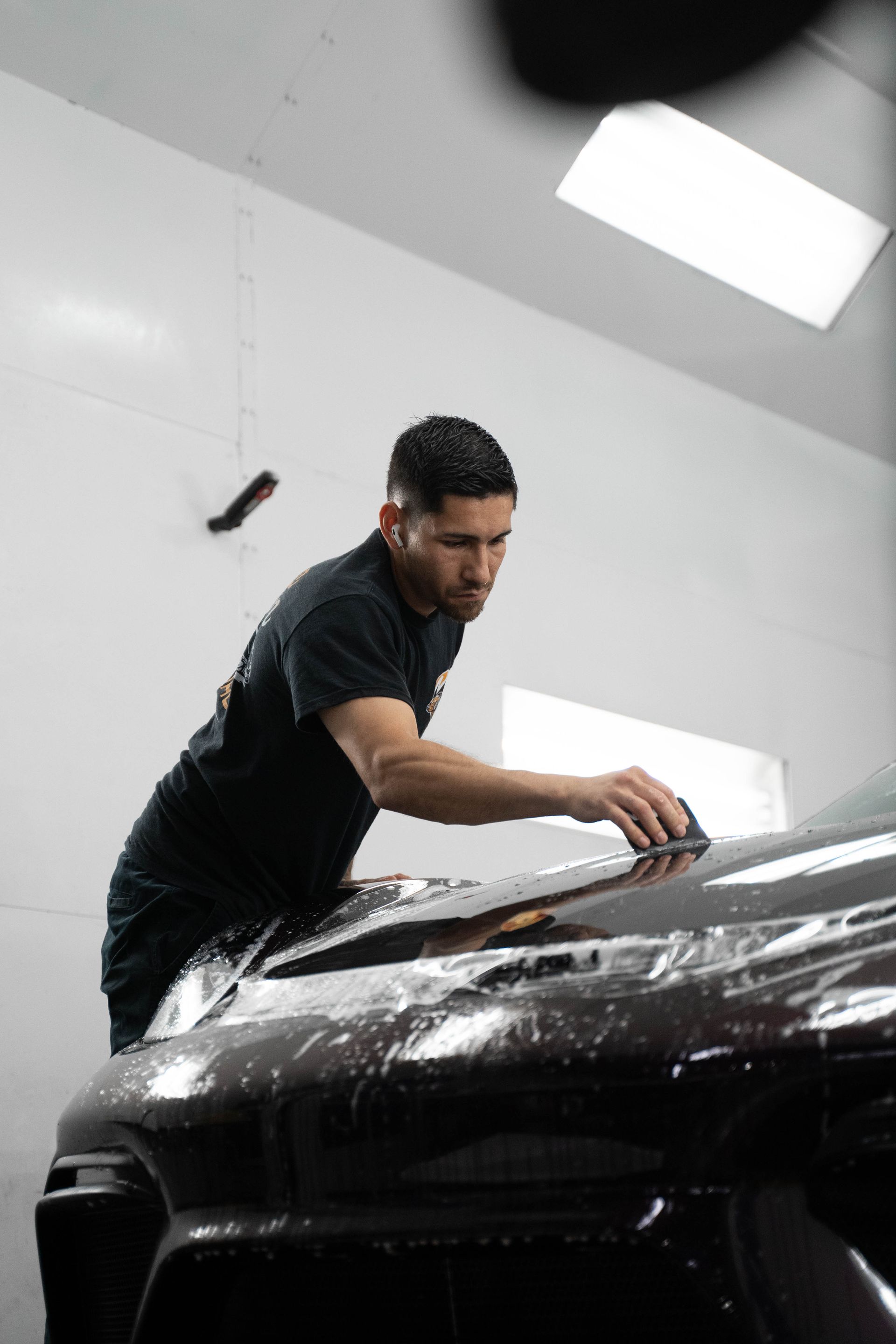 Man applying protective film to a dark car in a workshop.
