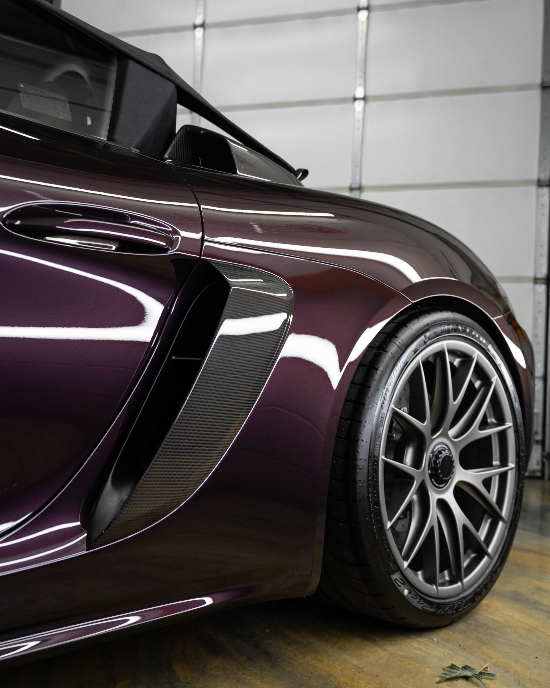 Dark purple sports car with carbon fiber air vent and gray alloy wheel.