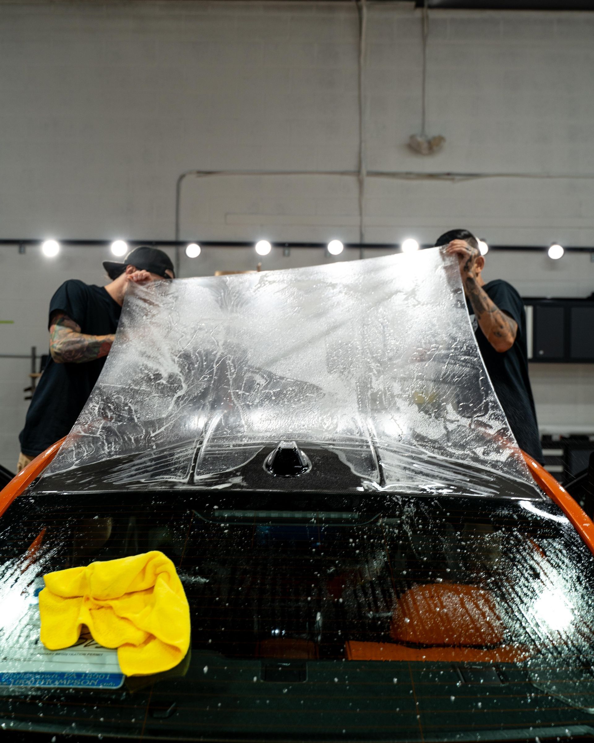 two men are wrapping a car with a clear plastic sheet .