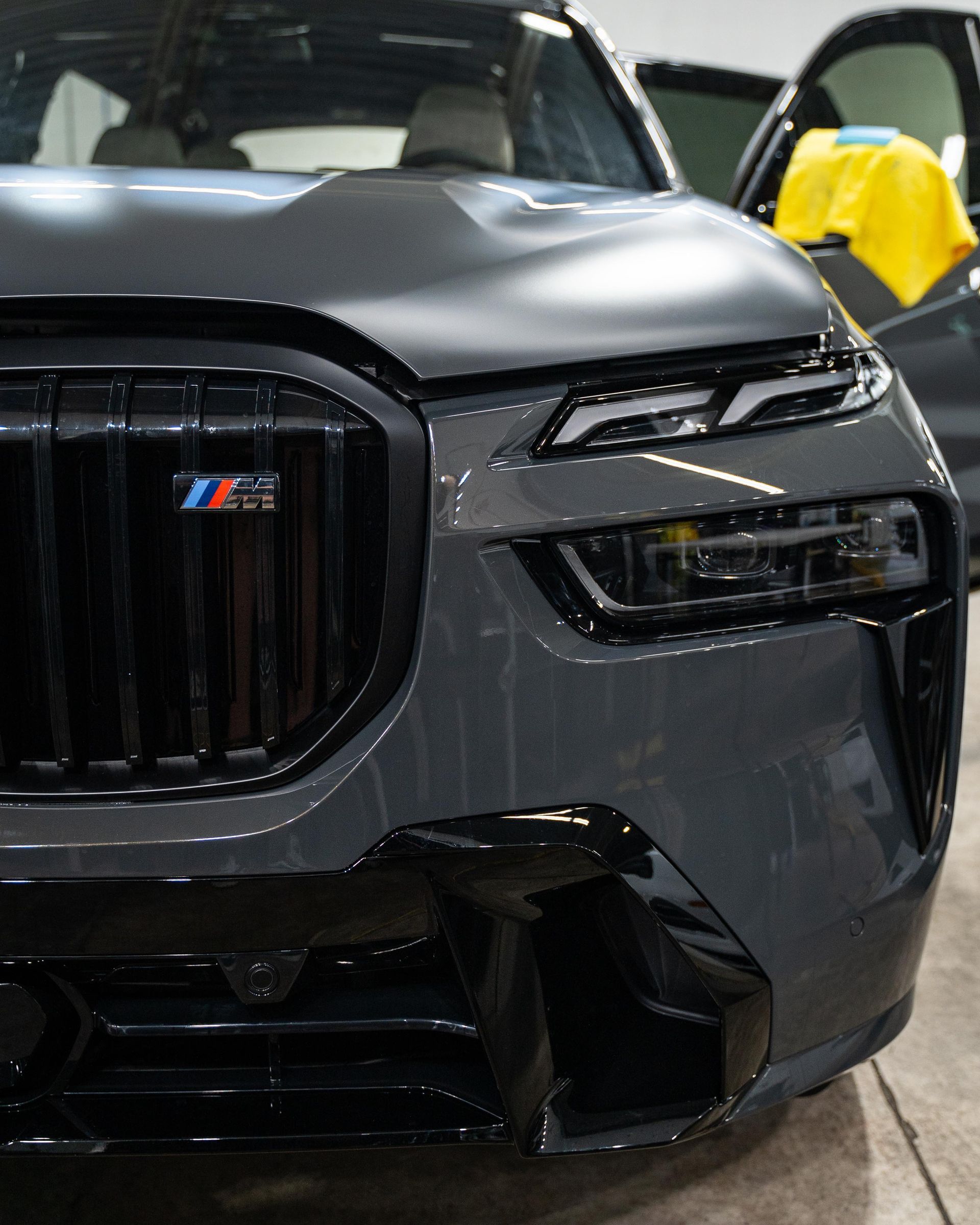 Close-up of a dark gray BMW SUV with a black grille, showing the front. The M logo is visible.