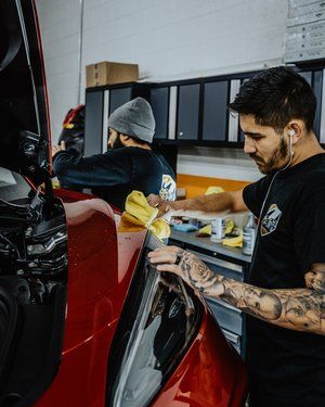 two men are working on a red car in a garage .