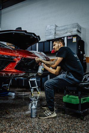 a man is sitting on a stool in front of a car in a garage .