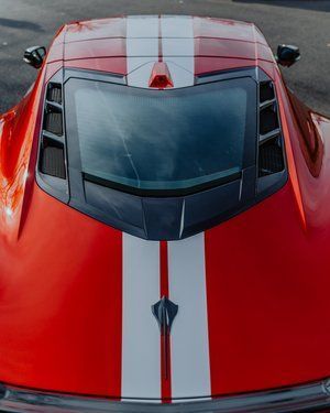 a red sports car with white stripes on the hood is parked on the street .