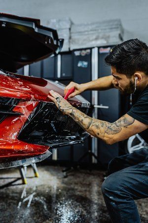 a man is working on a red sports car in a garage .