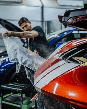 a man is covering a red car with a plastic bag .