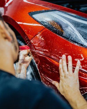 a man is applying a protective film to a red car .