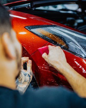 a man is wrapping a red car with a sponge
