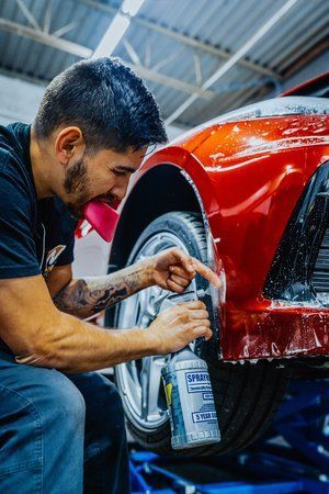 a man is cleaning the fender of a red car in a garage .