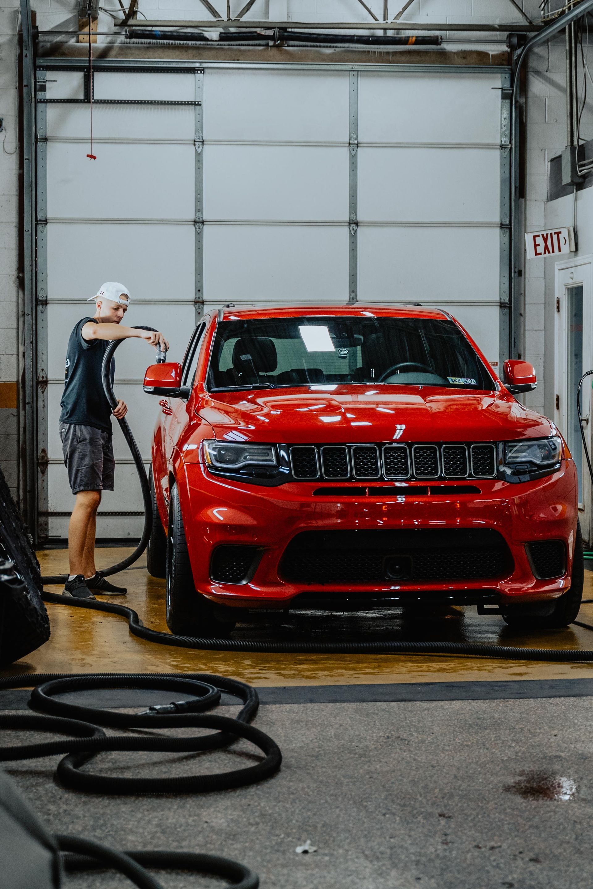 Person washing a bright red Jeep SUV inside a garage, using a hose.