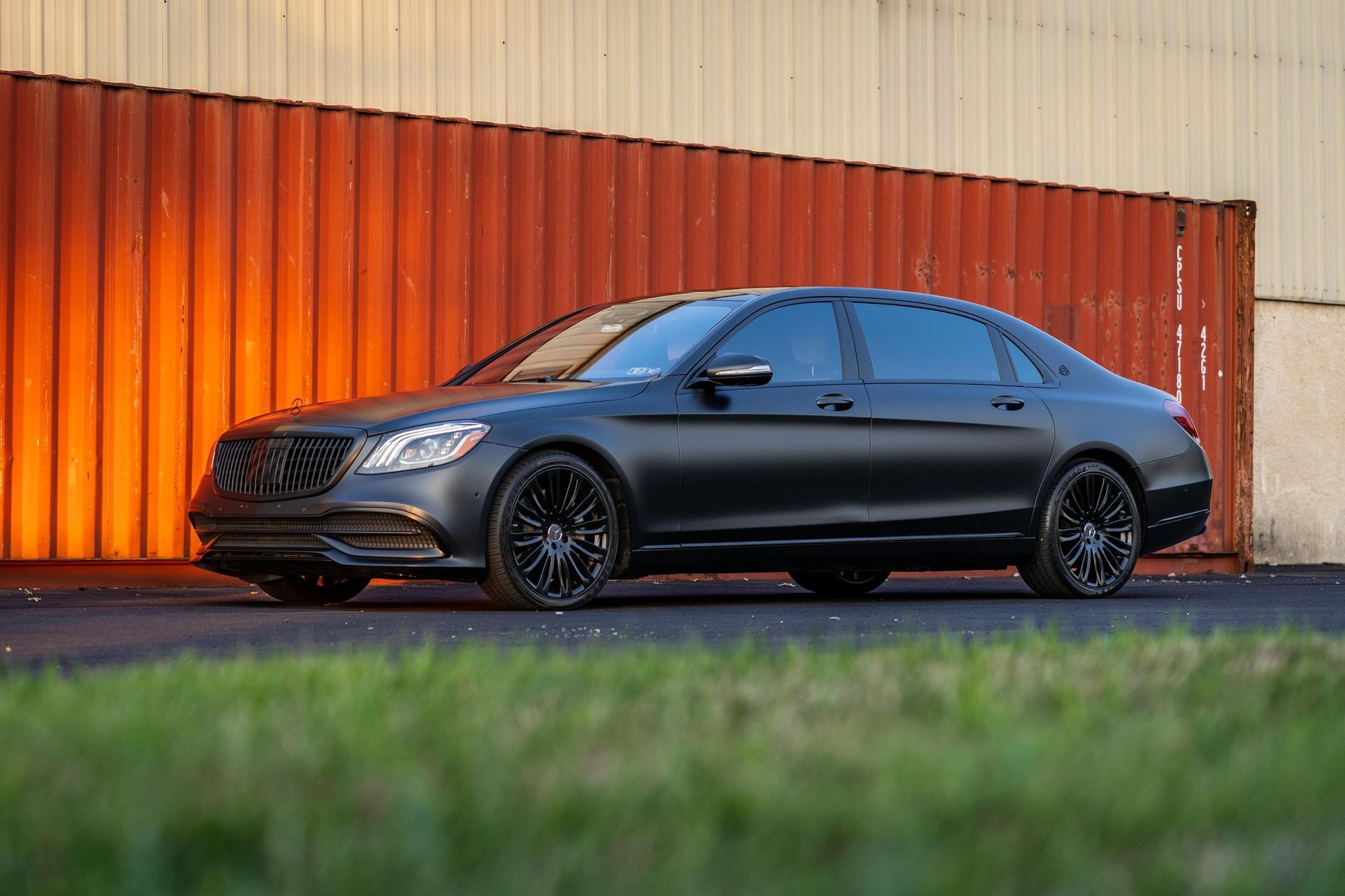 a black mercedes benz s class is parked in front of a red container .