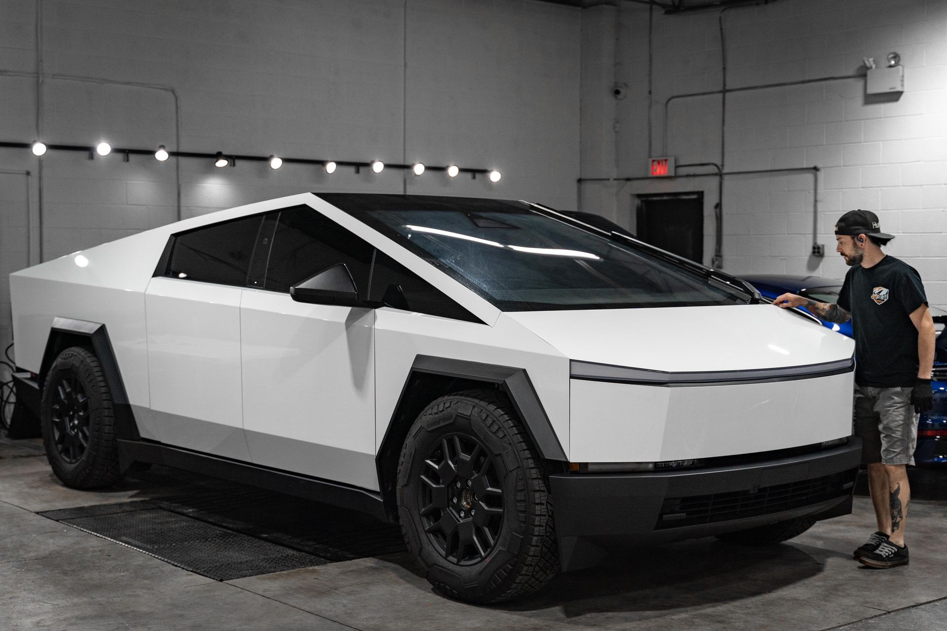 A man is standing next to a white tesla cybertruck in a garage.