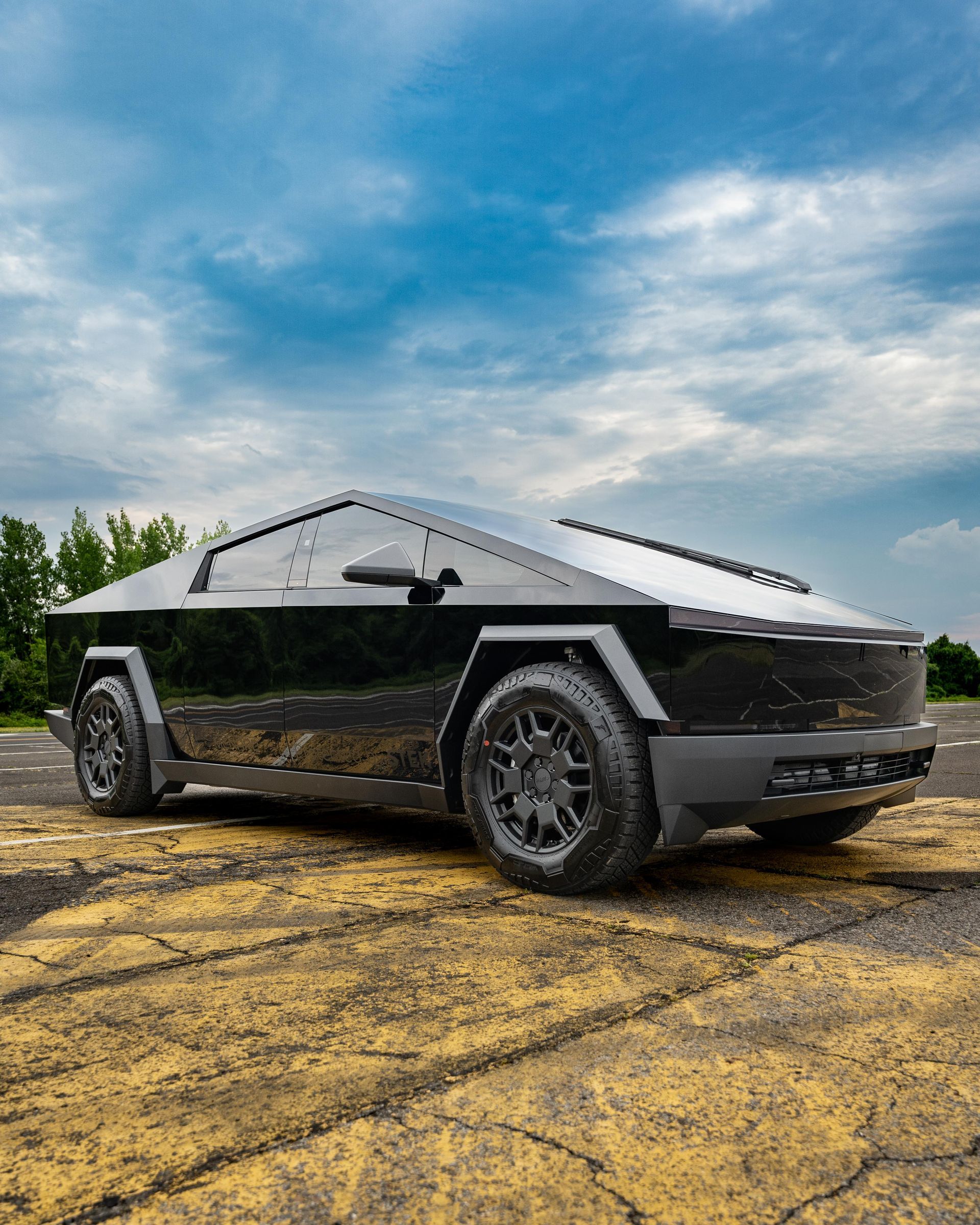 A black and white tesla cybertruck is parked on a dirt road.