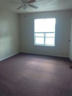 Empty room with burgundy carpet, window, ceiling fan.