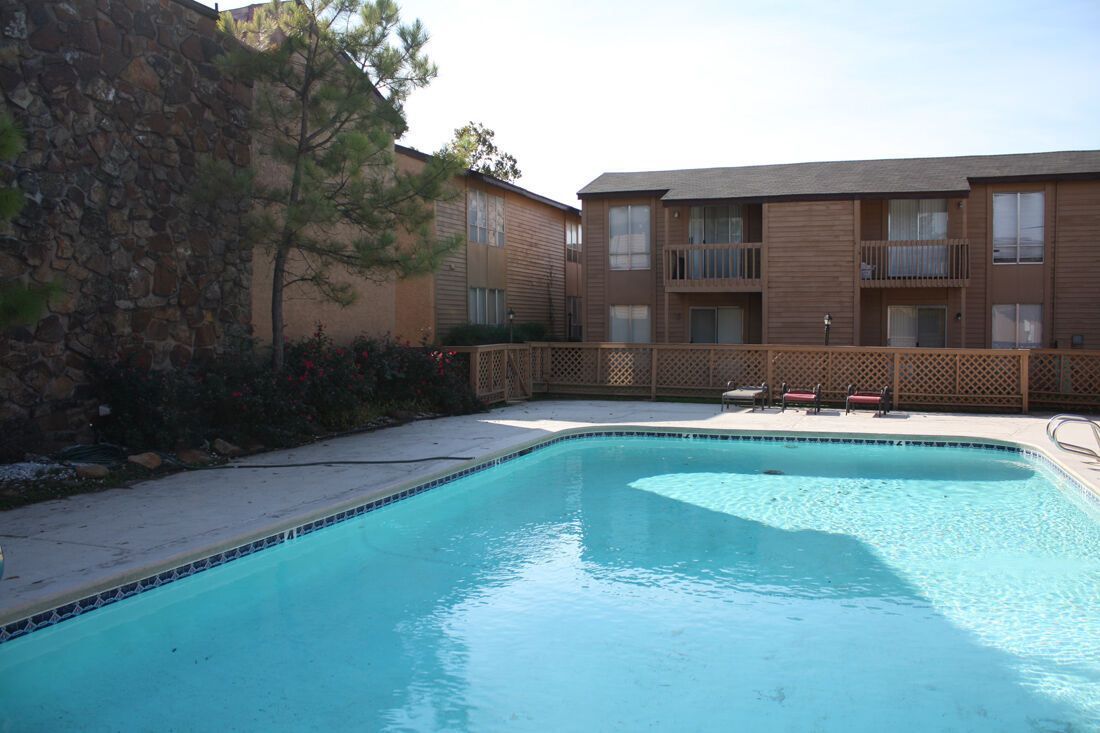 Apartment complex pool area with turquoise water, wood buildings, and a rock face on the left.