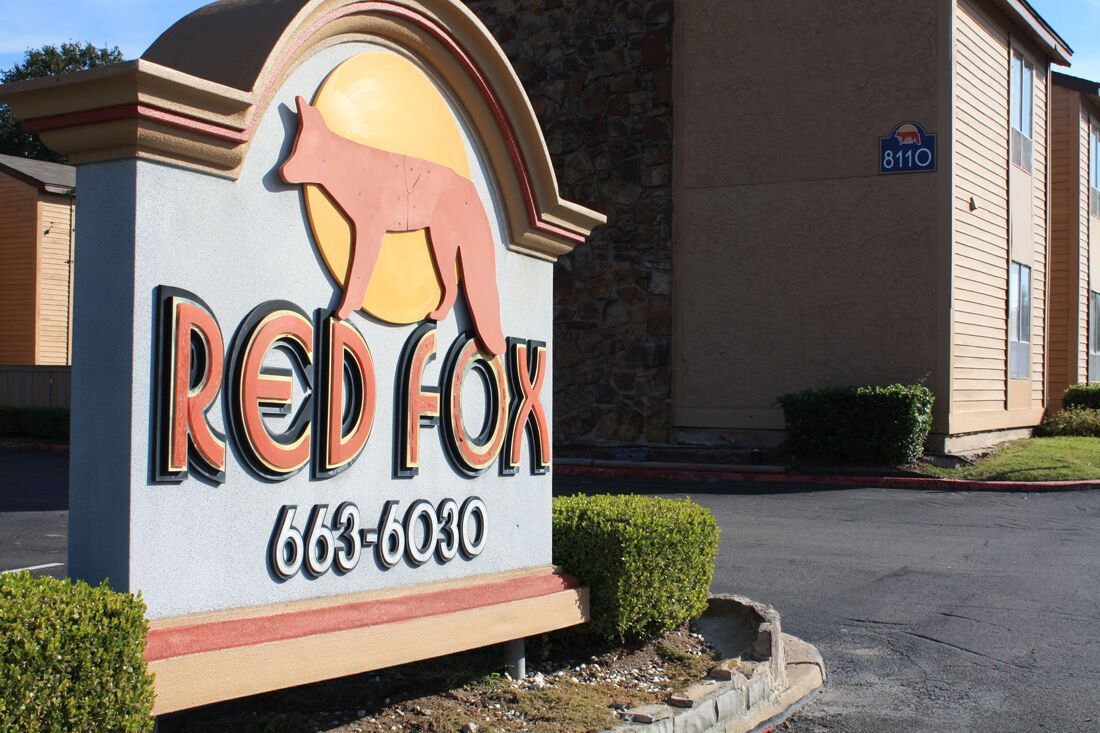 Sign for Red Fox apartments with a fox silhouette, phone number, and beige building.