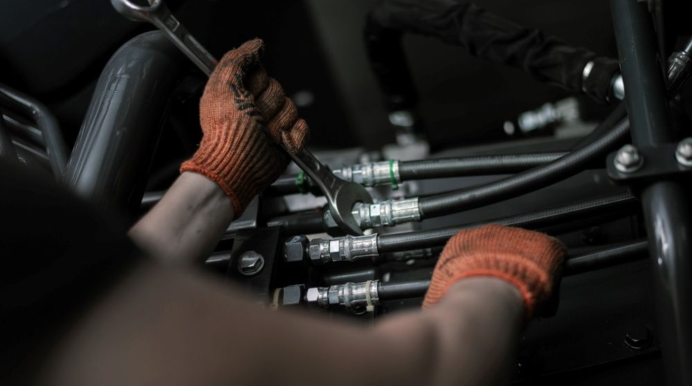 A Man Wearing Orange Gloves Is Working On A Machine With A Wrench — HI PSI Hydraulics in Wauchope, NSW