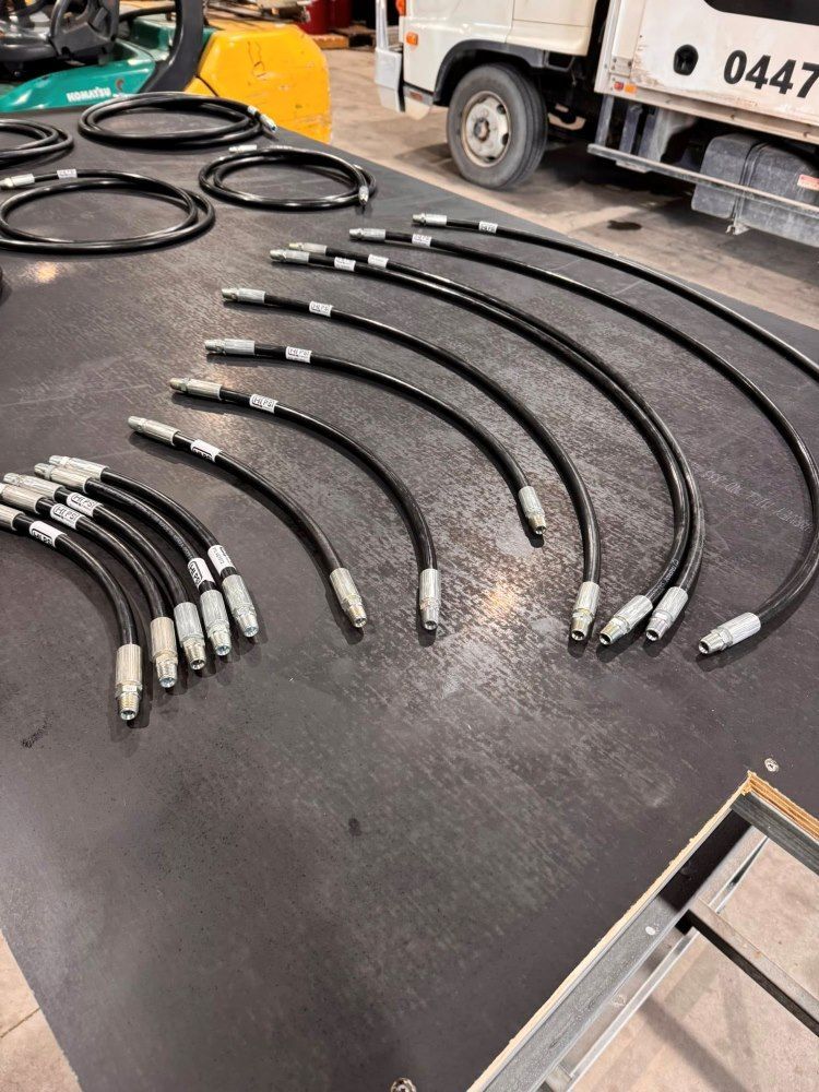 Black, curved hydraulic hoses with silver connectors, arranged on a dark surface. — HI PSI Hydraulics in Wauchope, NSW