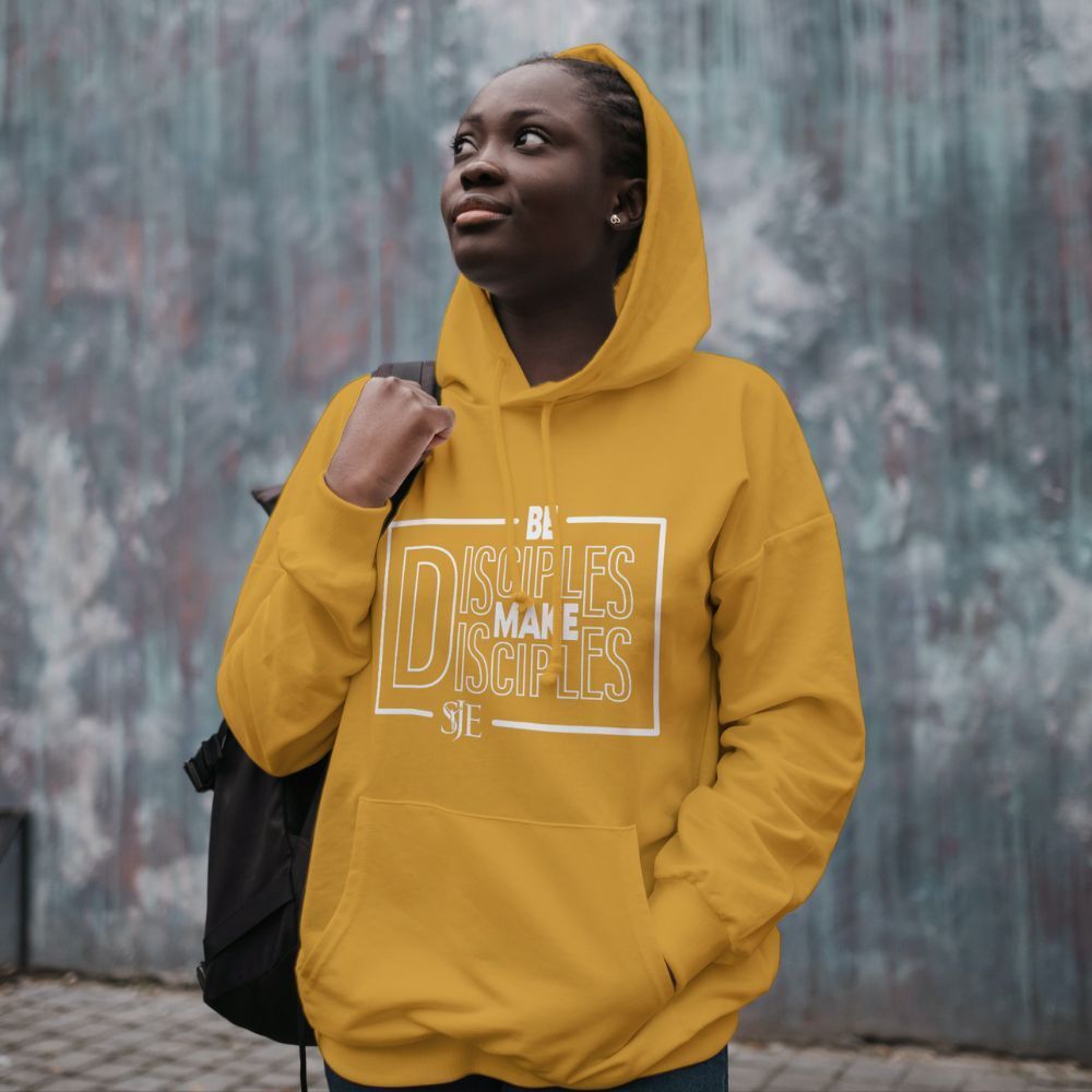 A woman wearing a yellow hoodie is standing in front of a wall. Be Disciples. Make Disciples.