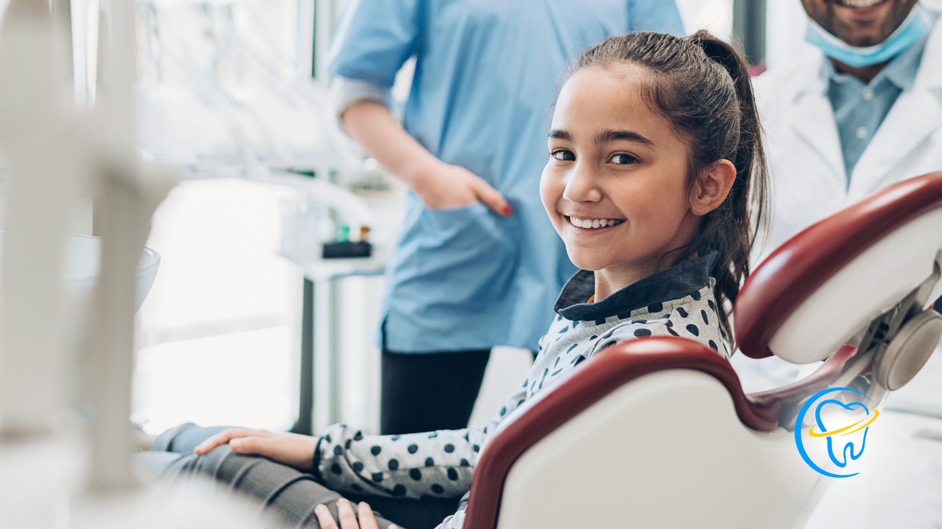 A young girl is sitting in a dental chair and smiling at the camera.