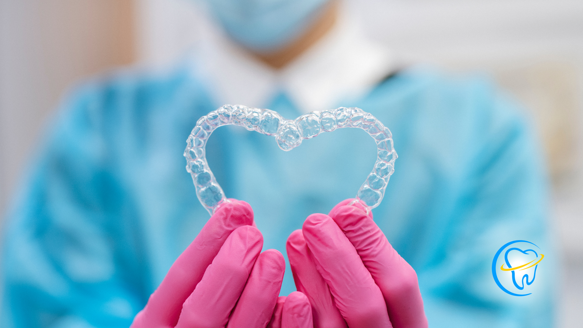 A dentist is holding a clear retainer in the shape of a heart.