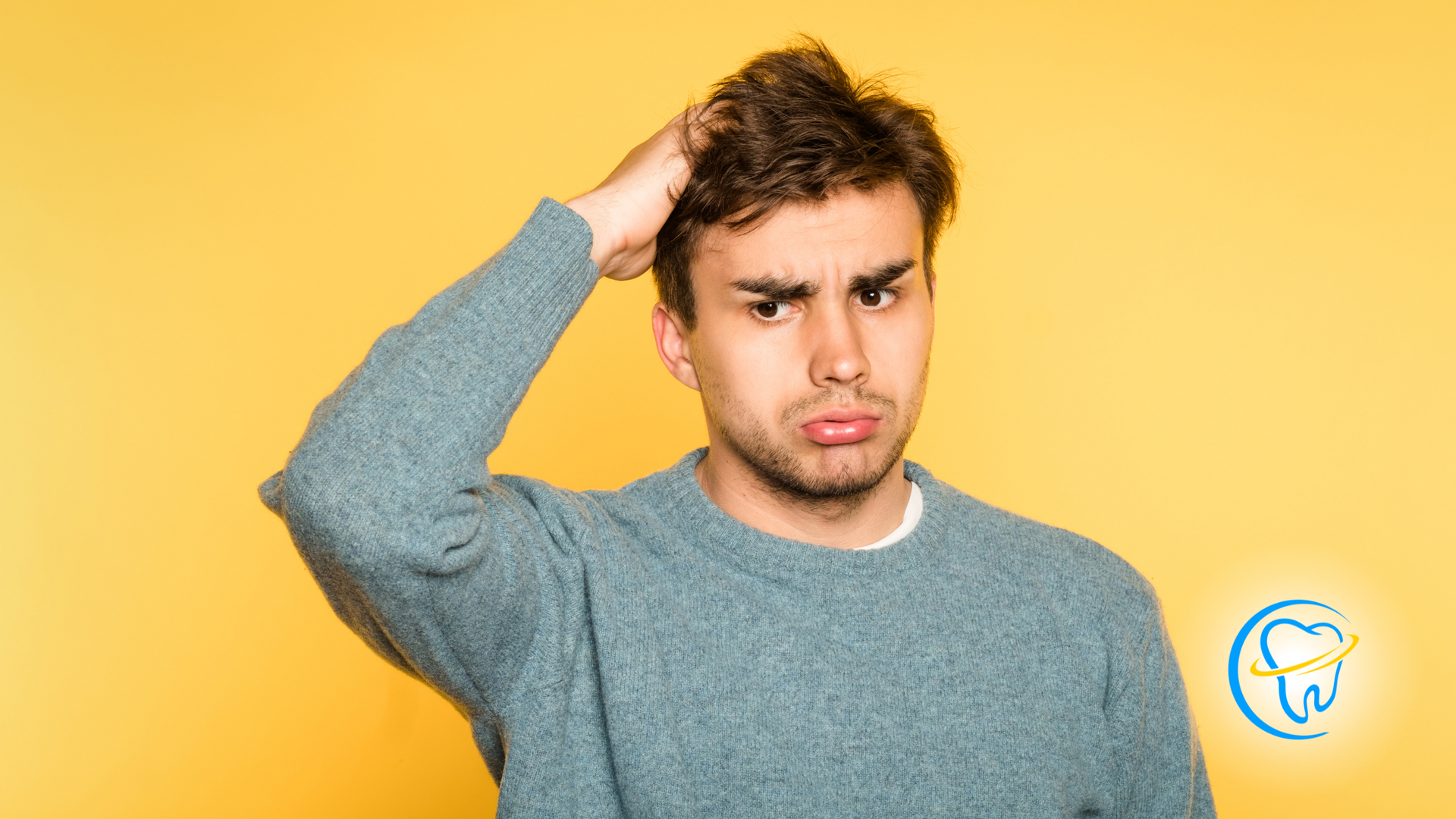 A man in a blue sweater is scratching his head.