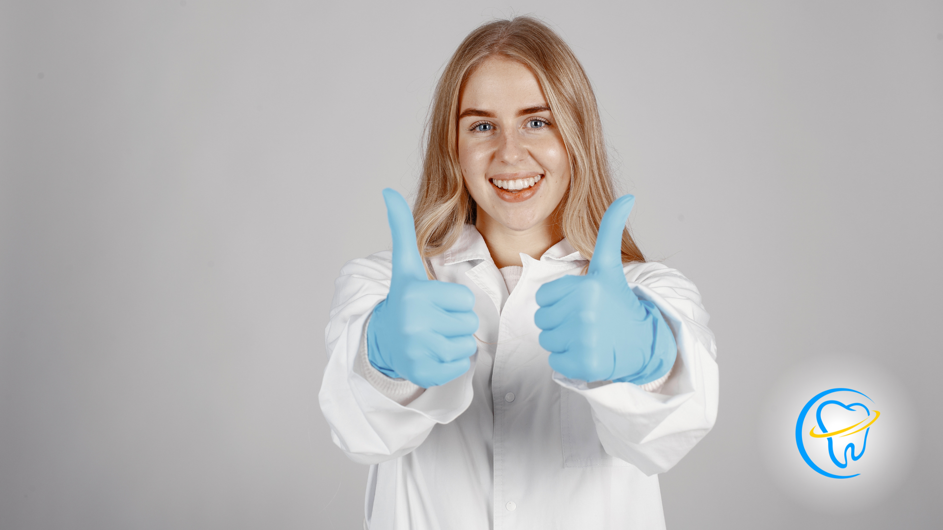 A woman in a lab coat and blue gloves is giving two thumbs up.